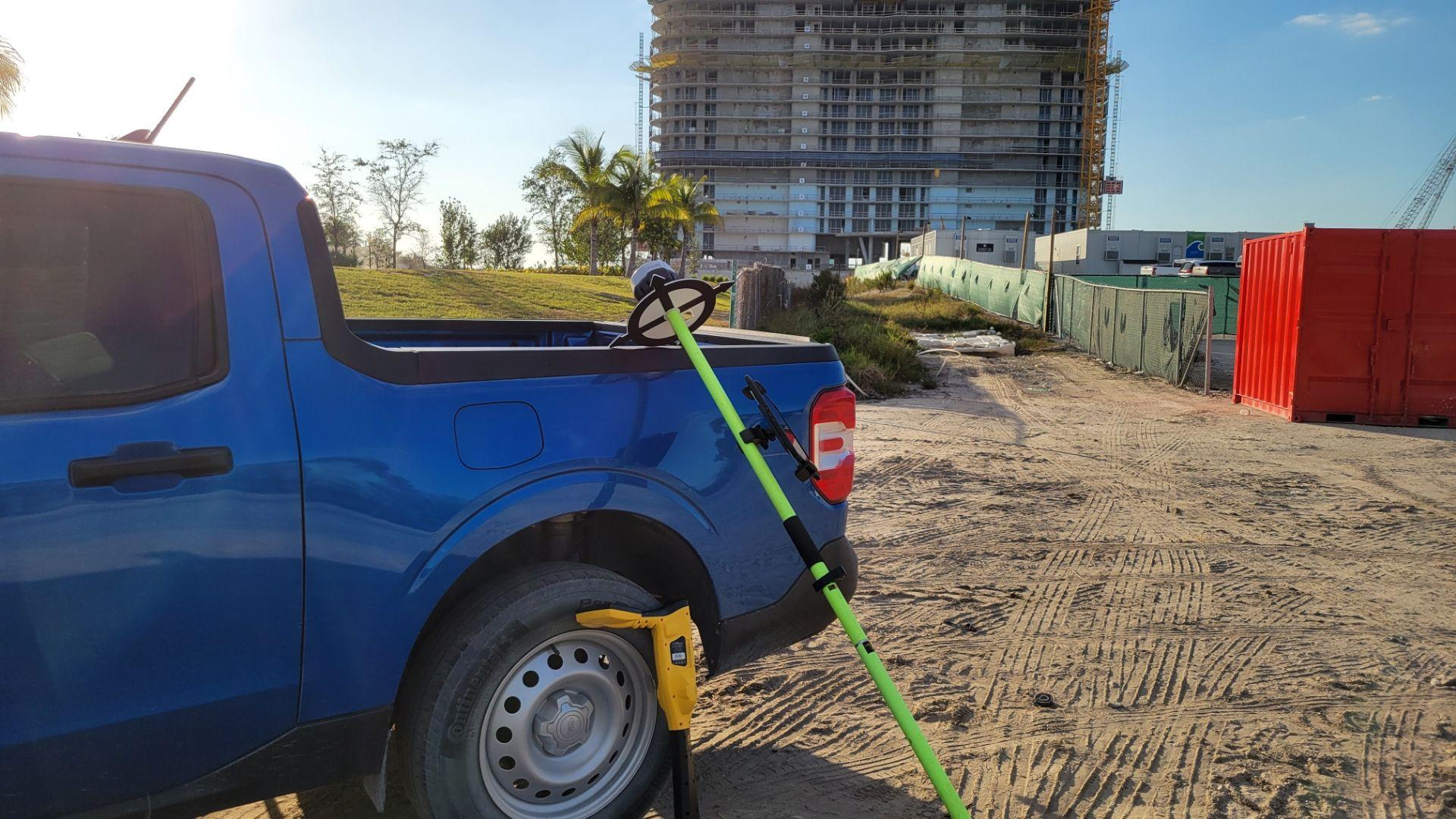 Blue pickup truck at a construction site with a large unfinished building in the background.