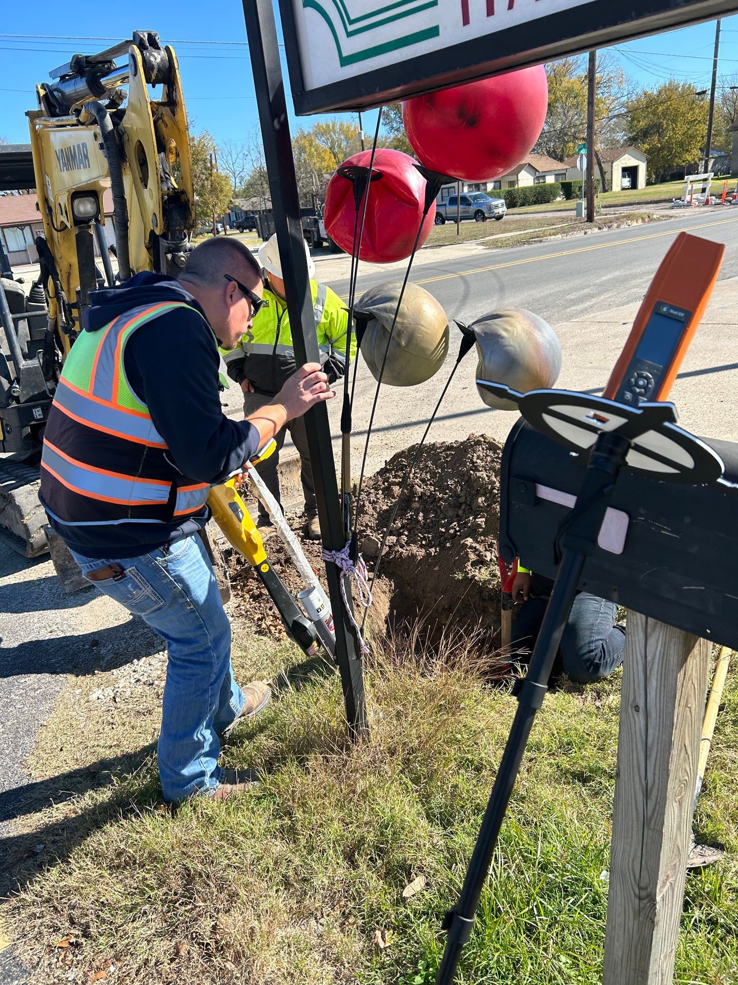 Workers using tools near a roadside sign with machinery and safety markers in the background.