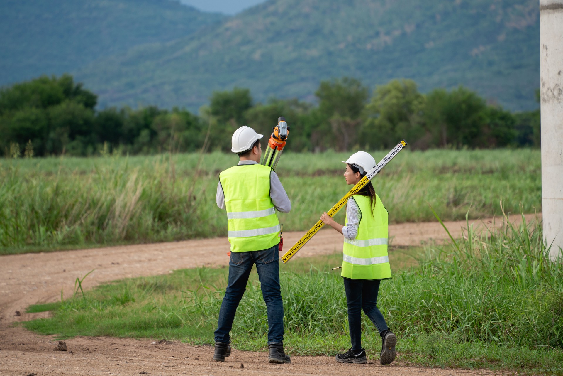 Two engineers wearing safety vests and holding surveying equipment