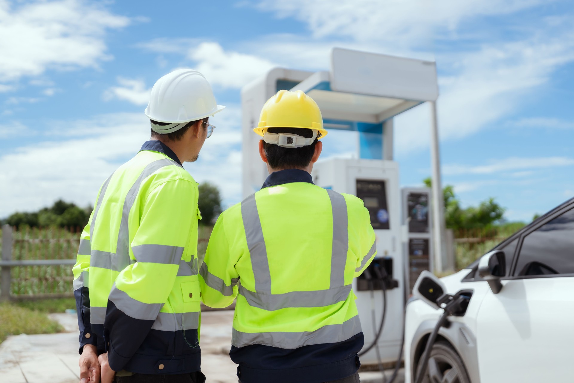 Engineers in safety gear discussing electric vehicle charging station installation at sunny outdoor site